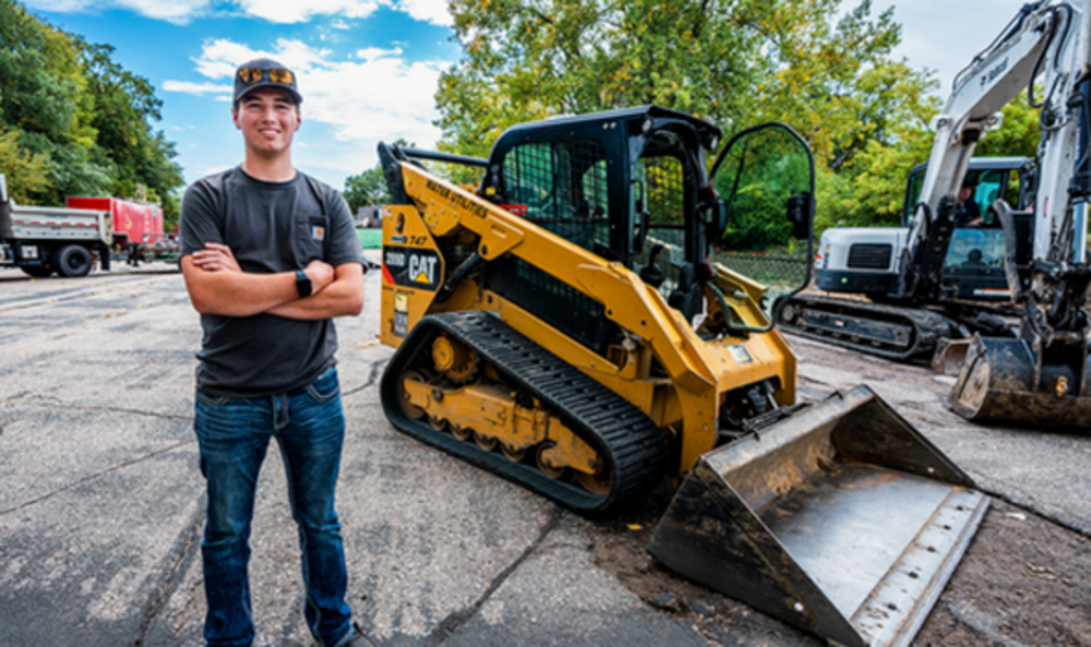 young man standing on a street next to machinery to fix roads