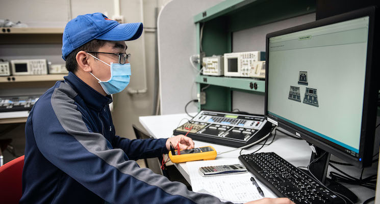 male student testing electronics functionality with tools and computer