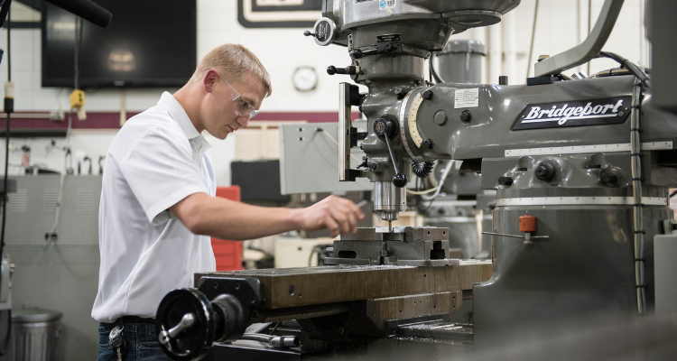 male student working on a drill press and setting up for production