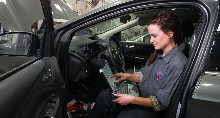 female automotive technology student running diagnostics on a laptop inside of a car