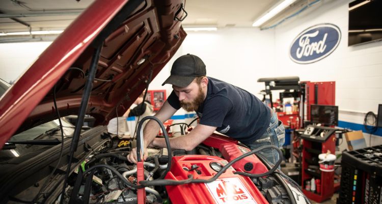 two students and instructor looking under the hood of a Ford vehicle