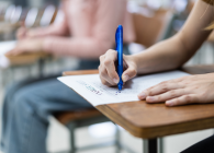 Student writing answers on a test paper in a classroom setting.