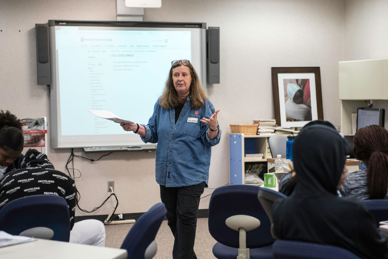 A female instructor lectures in front of a classroom full of students.