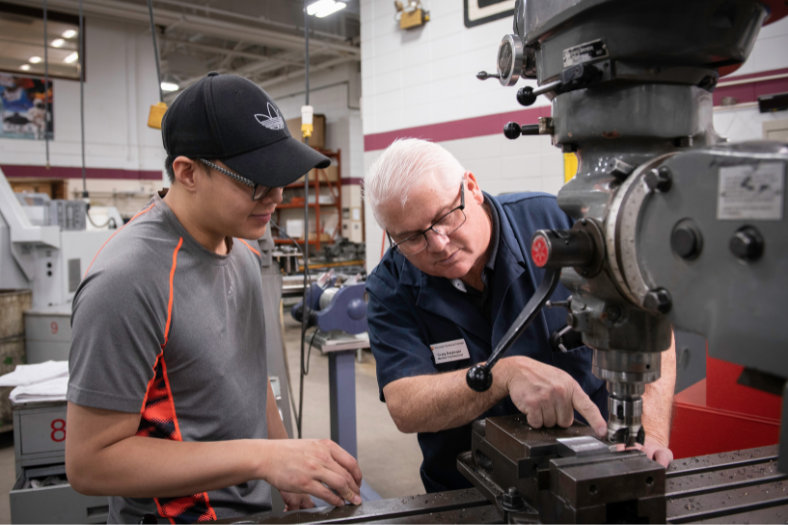 An instructor and student focus on the workings of a machine.