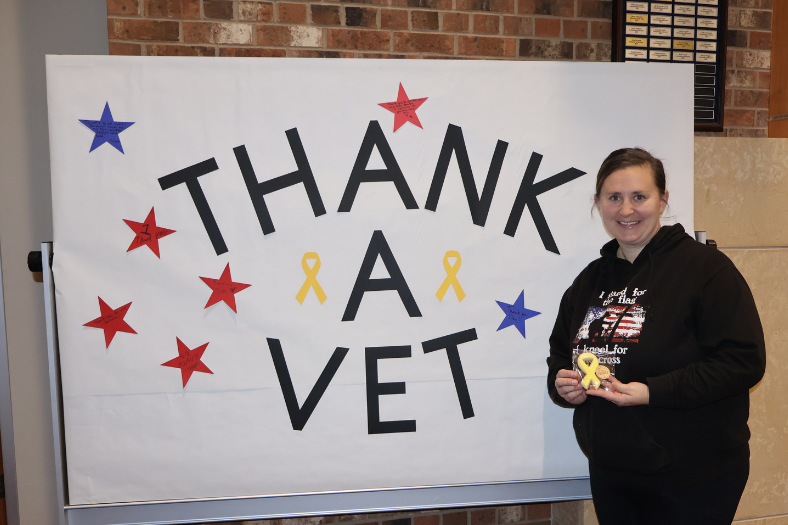 Anna Reiman posed in front of a board reading Thank a Vet with a cookie she made for the event